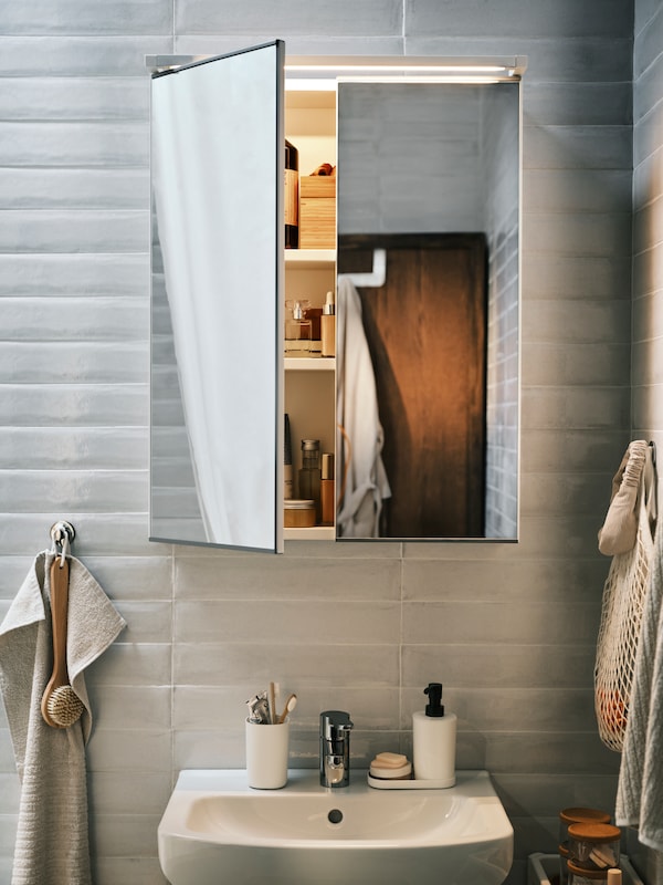 白色ENHET镜子内阁在一个洗脸盆,一扇门打开显示各种项目里面,加上浅肤色的手毛巾。