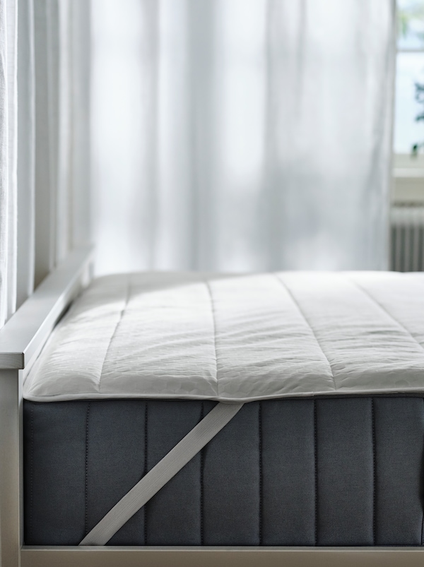 一张白色HEMNES床的一端，上面有一个VALEVÅG口袋弹簧床垫，上面覆盖着ROSENVIAL床垫保护器。