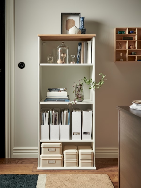 白色SKRUVBY书柜与装饰物品、文件存储盒和盖子和杂志站在白墙。