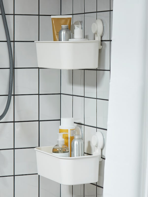 瓷砖浴室淋浴的角落里有两个TISKEN篮子，墙上有白色的吸盘，里面装着浴室用品。