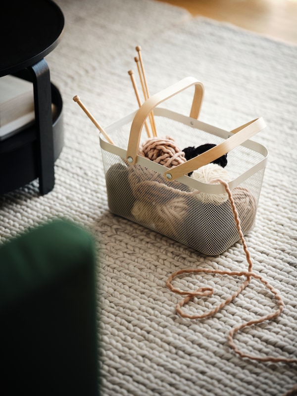 一篮子RISATORP与桦木处理坐在地毯在地板上,和球的羊毛针织针伸出。