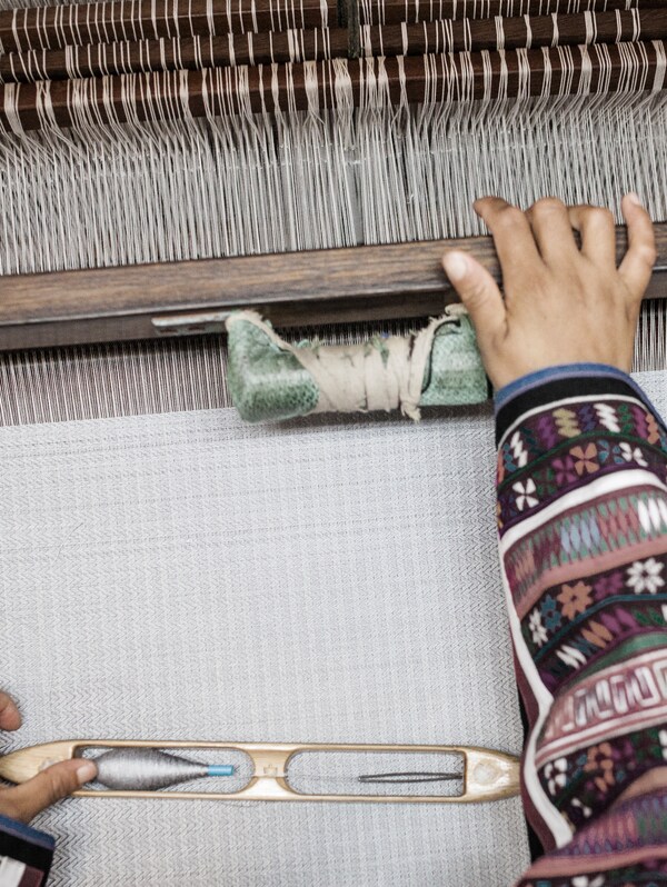 韦弗穿着传统图案的上衣的手在编织的过程中一个白色地毯织机。