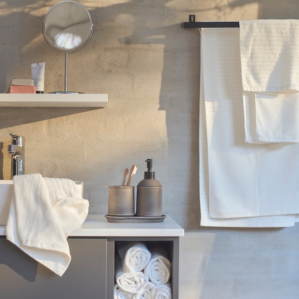 Väggen i ett badrum med en hylla med spegel på och vita VÅGSJÖN handdukar som hänger från en SKOGSVIKEN handduksstång。