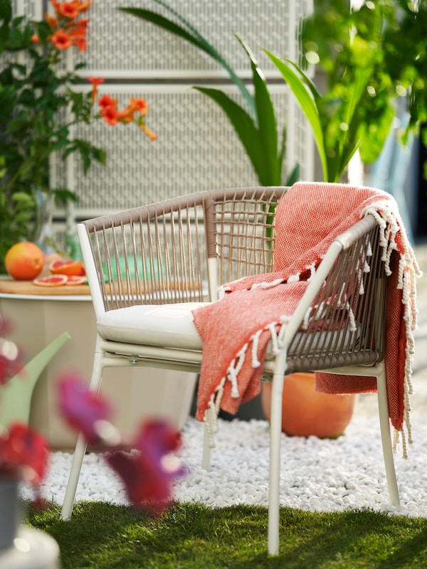 一个充满活力的扔在SEGERON椅子旁边LAGASKAR咖啡桌在砾石庭院点缀着鲜花和绿叶植物。