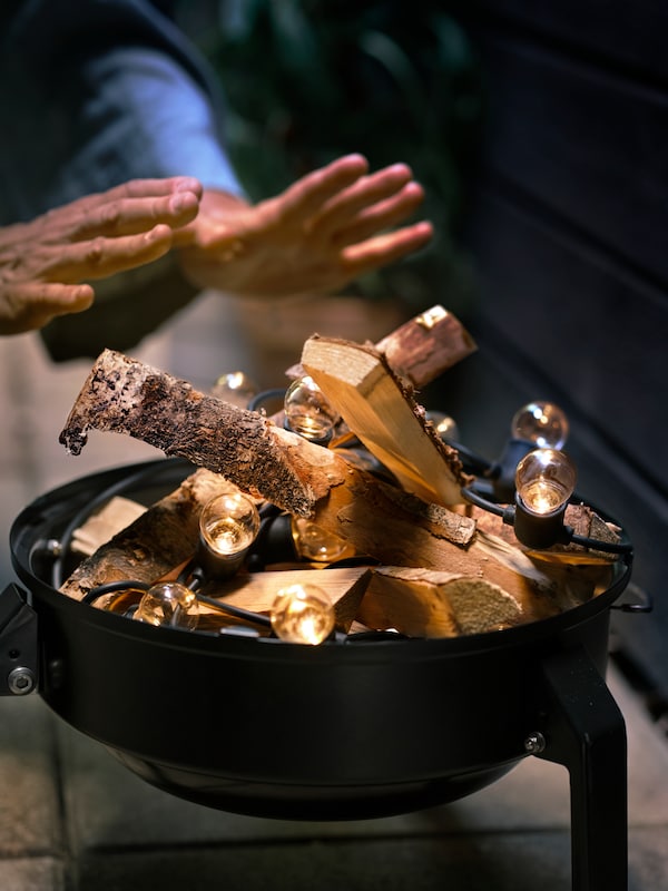 一双双手变暖在一个假的篝火的柴火和黑色UTSUND照明链在一个便携式烧烤。