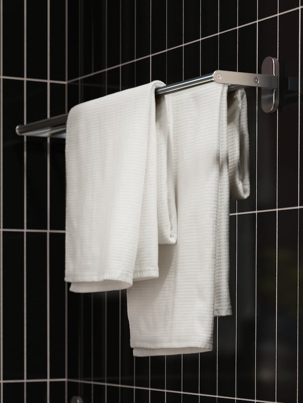 BROGRUND毛巾轨道安装在浴室墙壁穿着窄,黑色的瓷砖。铁路上挂着两条白毛巾。