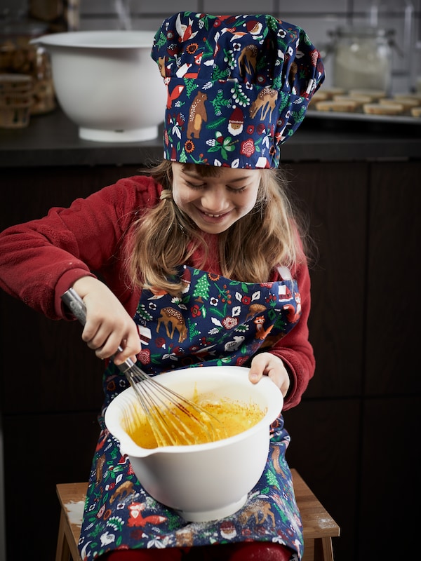 一个女孩在2021年酿造儿童hat-and-apron组合攻击面糊的白色VISPAD手动打蛋器搅碗里。