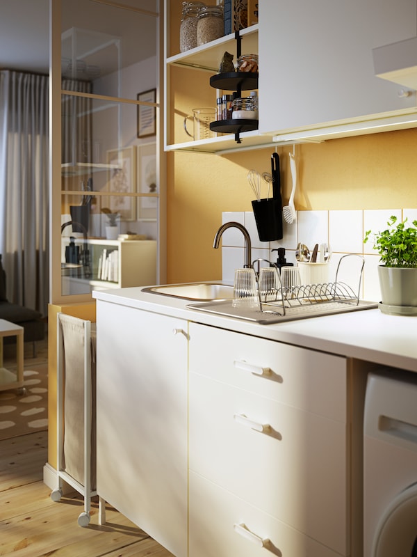厨房与黄色的墙壁,木制的地板和白色ENHET厨房方面。眼镜和餐具餐具滤干。