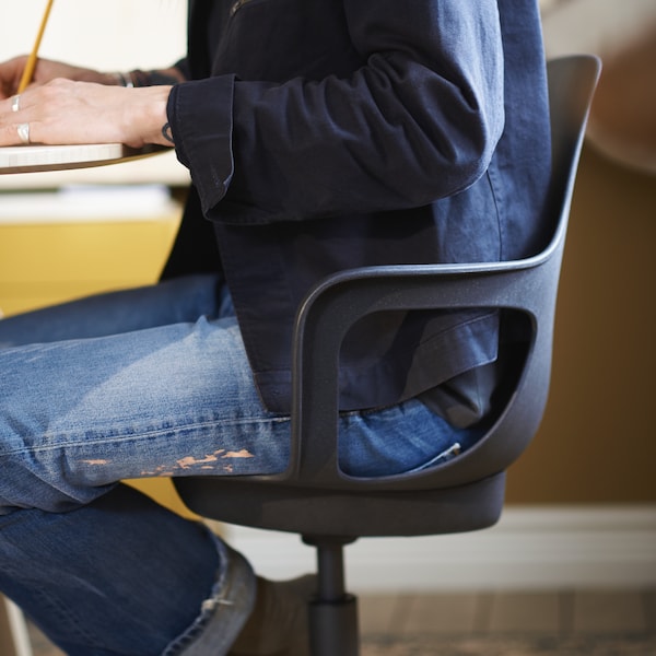 一杯人穿着牛仔裤和einem blauen Hemd sitzt一个einem Schreibtisch auf einem ODGER Drehstuhl。