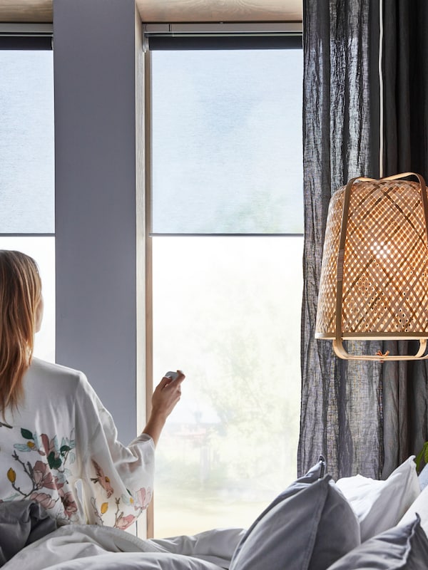 附近的一个女人,在床上KNIXHULT吊灯,使用远程控制KADRILJ卷帘挂在窗户。
