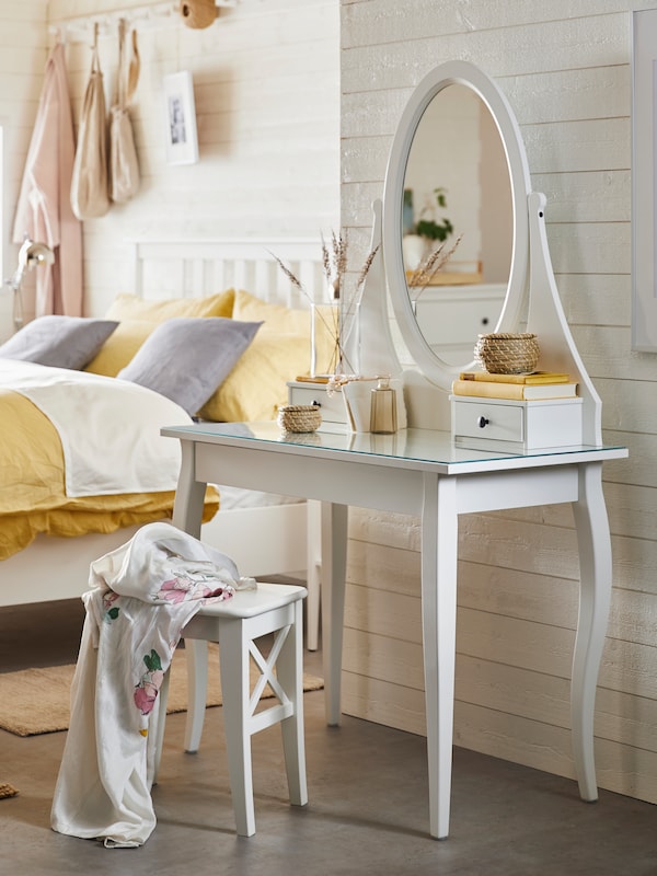 白色彩色HEMNES梳妆台镜子和一个白人INGOLF HEMNES附近的凳子站在卧室的床上。
