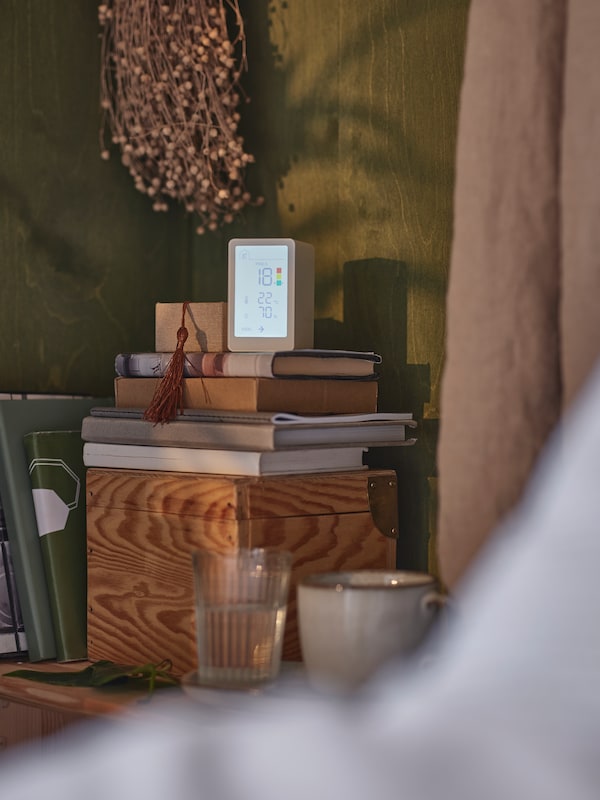 VINDSTYRKA空气质量传感器的一些书站在一个木盒子在玻璃和一个杯子在角落里。