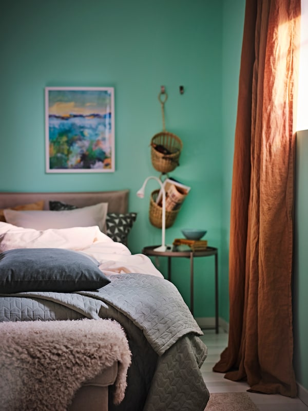 床由光grey-beige ANGSLILJA床单,床罩和各种垫子,一个窗口与黑暗的米色窗帘。