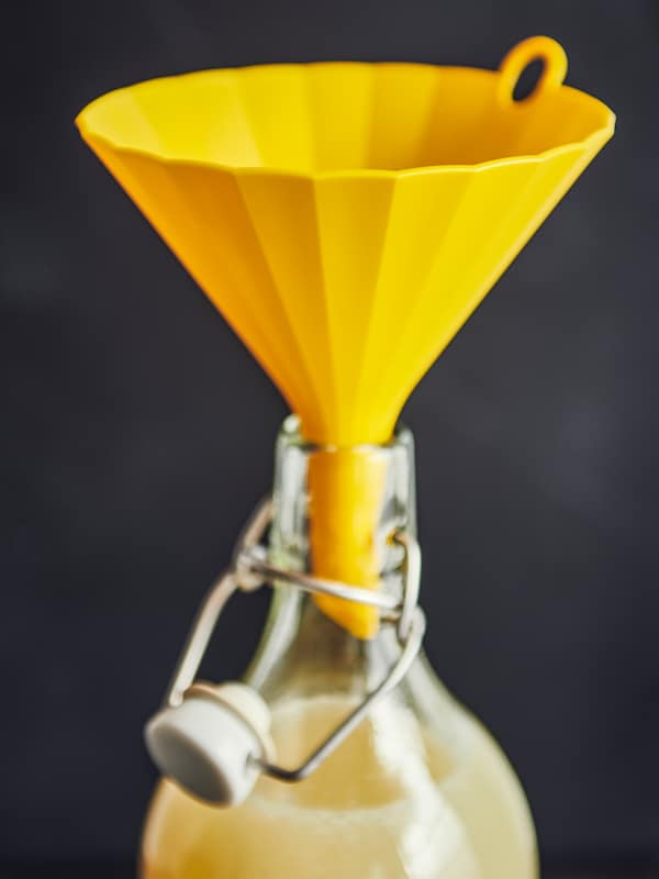 亮黄色的UPPFYLLD漏斗放在脖子上的一瓶KORKEN与塞在清楚玻璃,液体瓶子里。