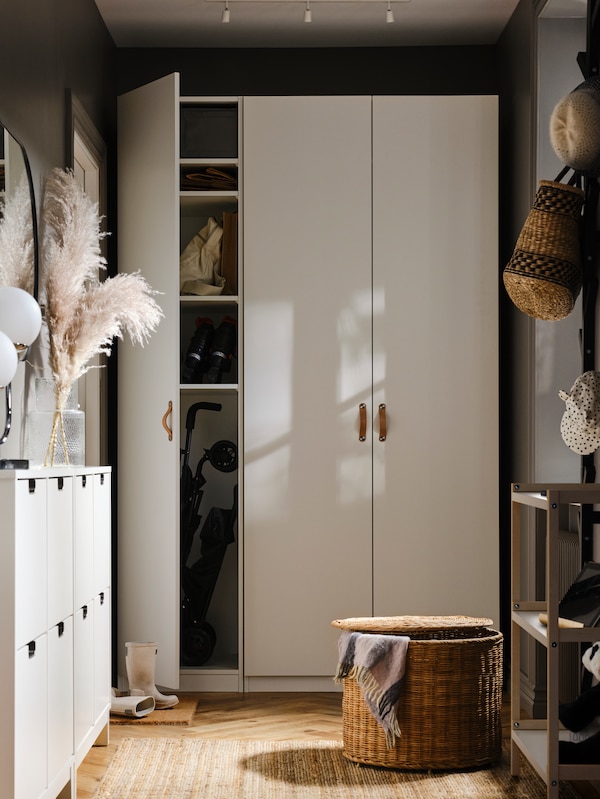 白色罗马/ FORSAND衣柜的一条狭窄的走廊里包含两个白色摊位鞋柜子和藤大坐垫。