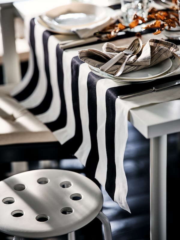 角落里的一个装饰华丽的表与白色OFTAST盘子和米色UPPHOJD餐具。下站着一个白色马吕斯凳子。