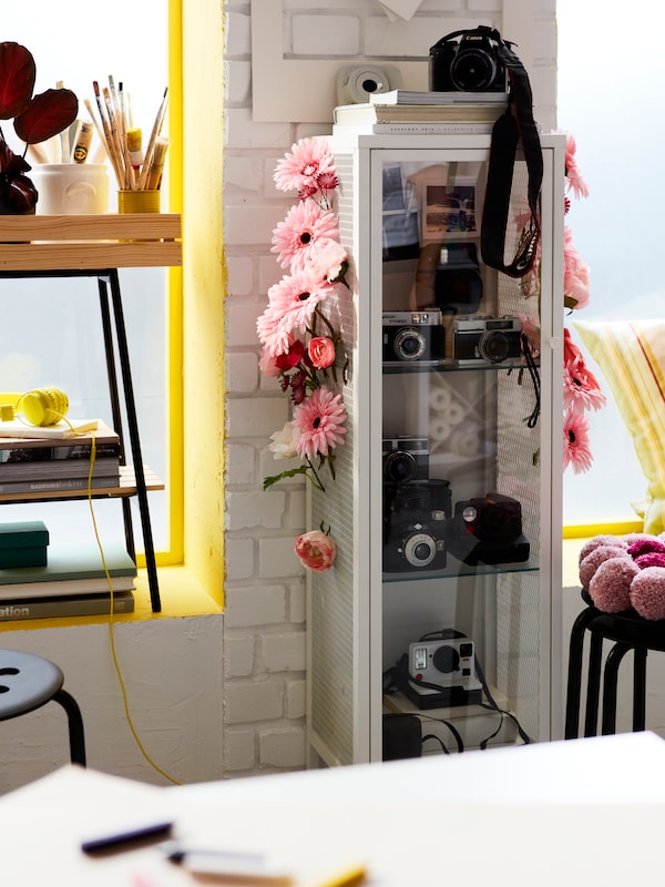 一个装满相机的BAGGEBO柜子，上面装饰着粉红色的SMYCKA人造花。