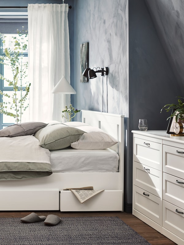 SONGESAND床2存储盒蓝色的卧室里覆盖着白色的床单和绿色和浅灰色坐垫上。