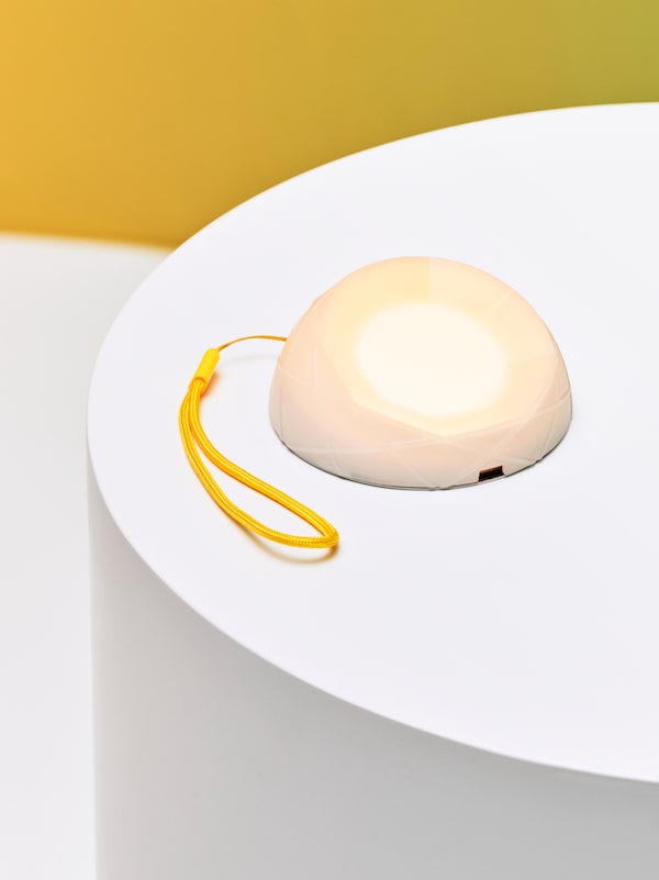 SAMMANLANKAD LED太阳能照明和黄色腕带坐在白色表和一个黄色的墙后面。