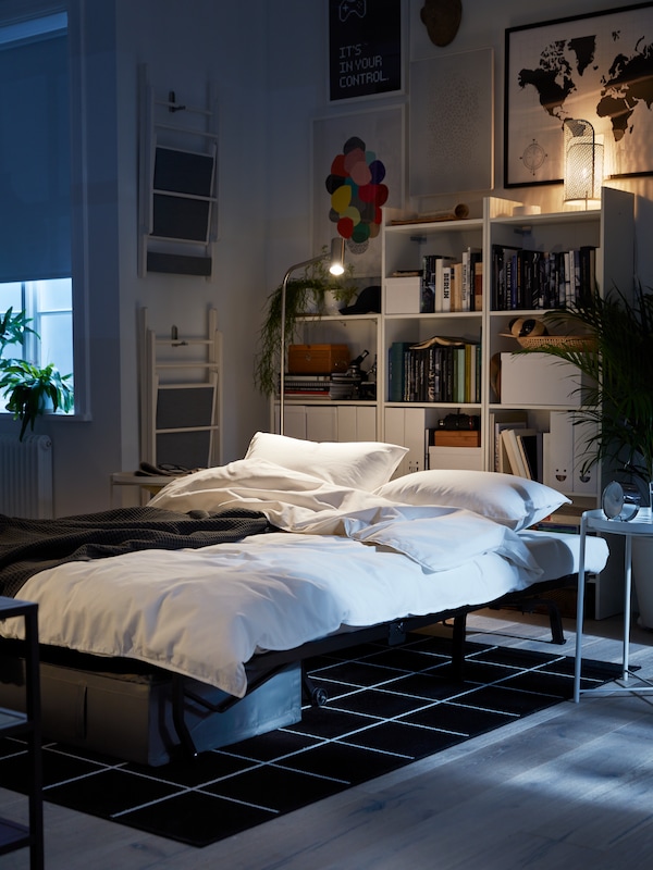 2-seat床折叠的床上,白色的被套和枕套,白色的书架,墙上的艺术。