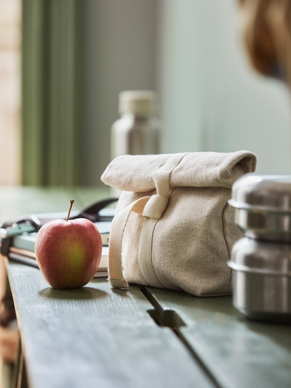 一个封闭HAJMAL零食袋在天然纤维中,站在PERJOHAN板凳旁边一个苹果和一个LATTUGGAD零食容器。