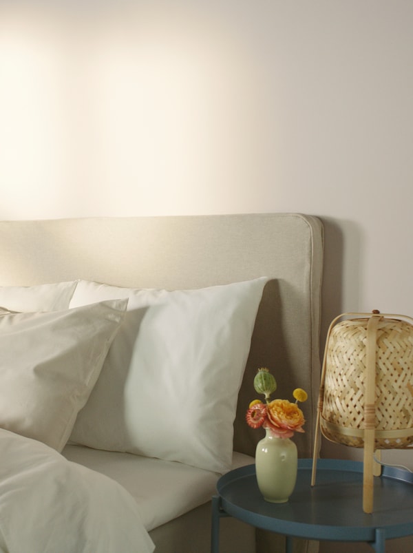 KNIXHULT竹灯和花瓶的花在桌子在床的角落里穿着白色棉质,DVALA床上纺织品。