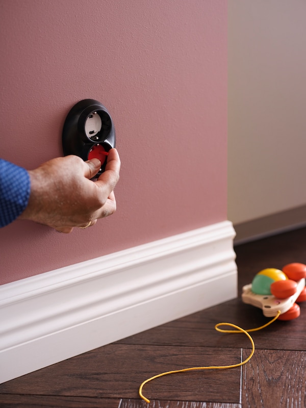 一个人把白色PATRULL安全插头从墙上的插座使用的工具,加上拉玩具在地板上。