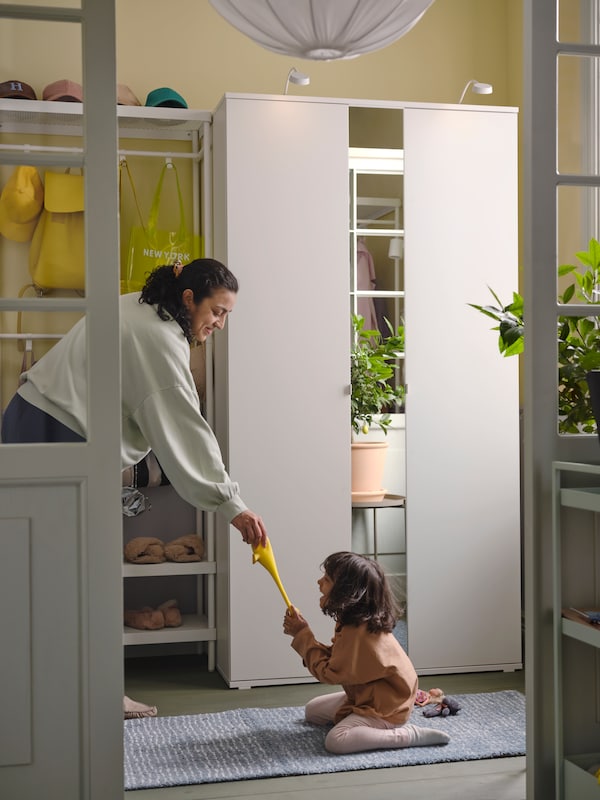 一个成人和一个孩子把一个黄色的玩具在前面VIHALS衣柜和MACKAPAR外套和鞋架存储。