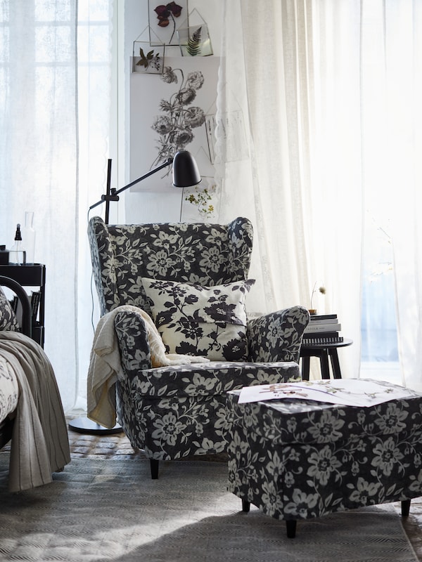 一个STRANDMON wingchair STRANDMON的脚凳,与花Frorum沙发套,站在一个阳光明媚的房间,窗帘。