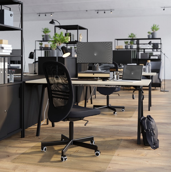一张TROTTEN桌子和黑色FLINTAN办公椅，在一个明亮的开放式办公室中，该办公室被划分为开放式书架和橱柜。