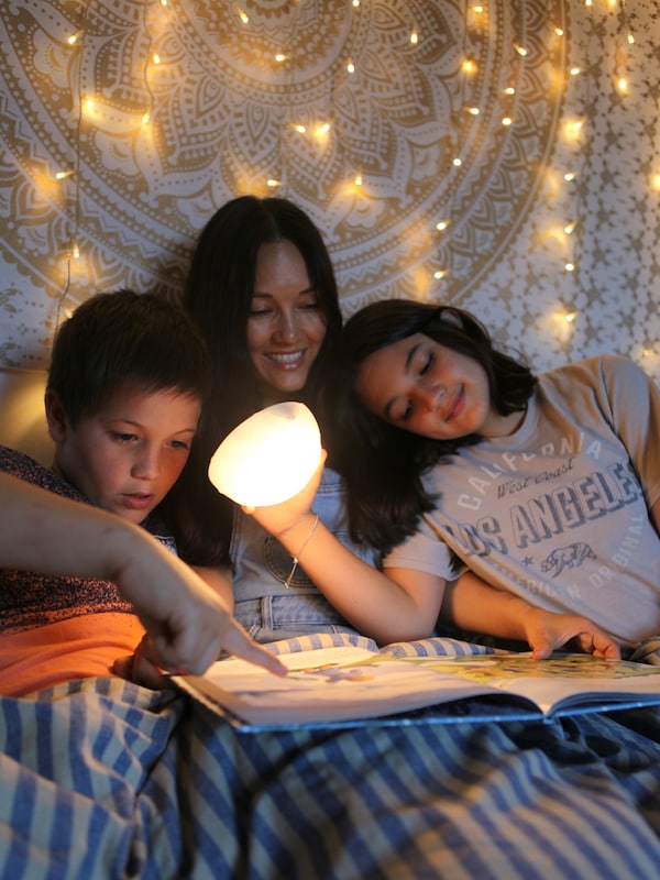 一个成年人和两个孩子坐在床上看书SAMMANLANKAD LED太阳能台灯的光源。
