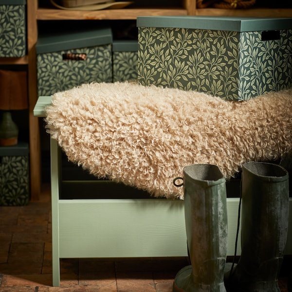 一张绿色的PERJOHAN木凳，上面有STUTERI储物箱和SVINDINGE合成羊皮地毯。