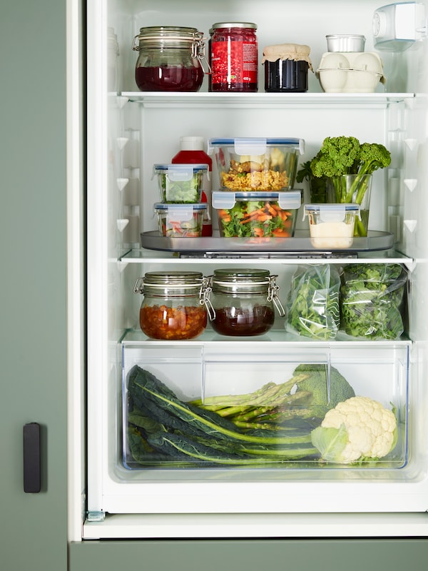 开放的冰箱装满了蔬菜,罐子和食品容器,其中一些被放置在转盘SNURRAD存储。