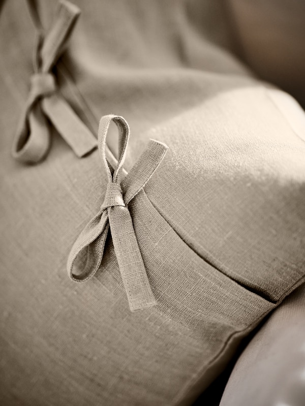 的米色AINA奶油沙发垫,显示两个紧固件系成的蝴蝶结装饰。