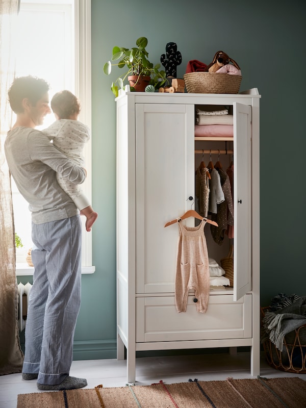 一个人站在窗户旁边面前举着一个婴儿白色SUNDVIK开着一扇门衣柜。