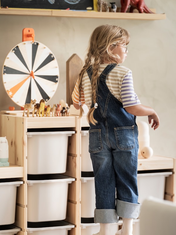 一个小孩站在一个TROFAST存储组合LUSTIGT wheel-game旋转,动物玩具。
