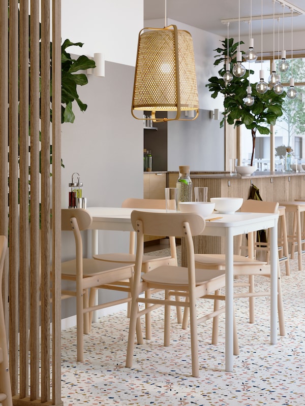 餐厅内部灯光明亮，白色的TOMMARYD桌子和RÖNNINGE桦木椅子下的KNIXHULT竹制吊坠。