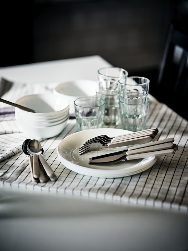 一个表与茶巾,盘子,盘子和水杯,刀子,叉子和勺子UPPHOJD餐具。