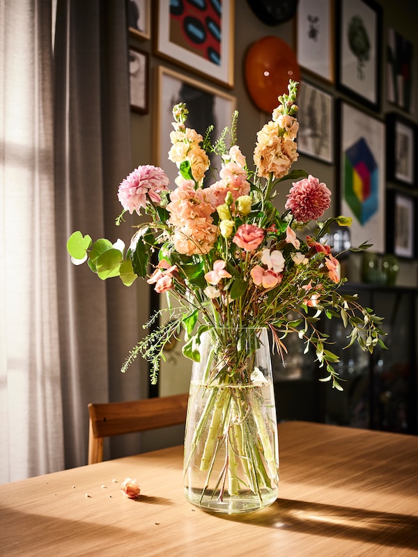 一束鲜花在BERAKNA透明玻璃花瓶DANDERYD橡树单板餐桌上灰色的窗帘的窗口。