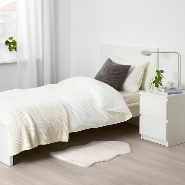 Eine TOFTLUND Matte vor einem MALM Bettgestell和einem MALM Ablagetisch在einem Weiss gehaltenen Schlafzimmer。