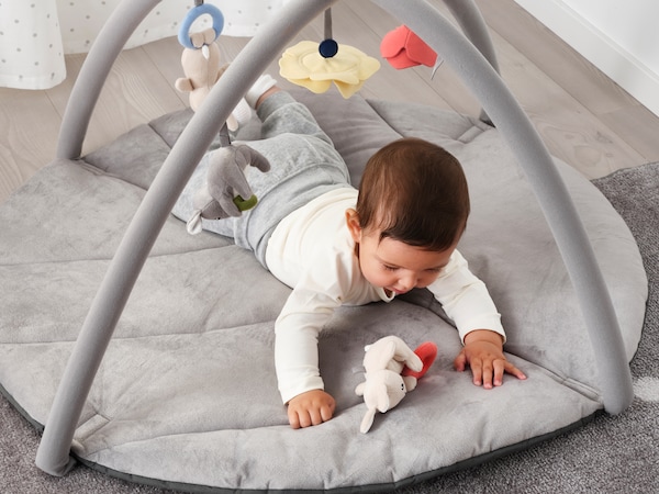 婴儿躺在一个灰色GULLIGAST婴儿健身小白色的毛绒玩具。
