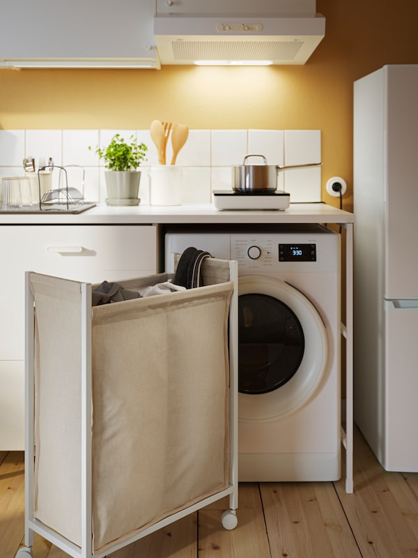 洗衣设置在厨房里白色的瓷砖和黄色的墙壁。旁边有一个白色ENHET洗衣袋一台洗衣机。