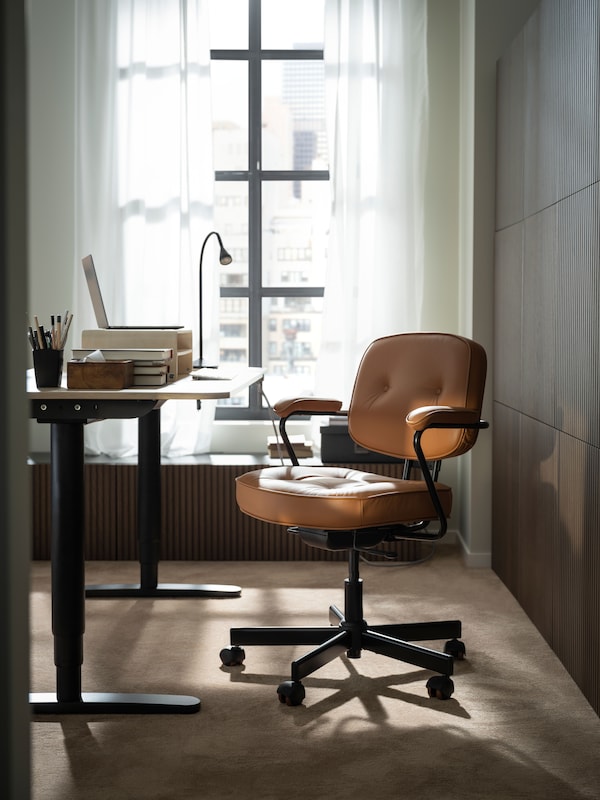 一个工作区,通过一个大窗户,阳光的oak-veneer BEKANT坐立桌子和金ALEFJALL办公椅。
