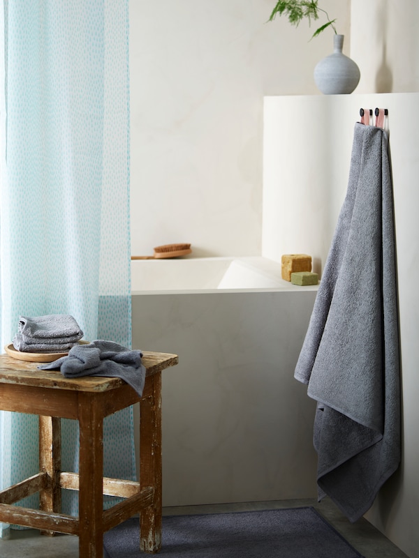 Ett badrum med Ett vitt och turkost duschdraperi över Ett hörnbadkar, med flera DIMFORSEN handdukar i närheten。