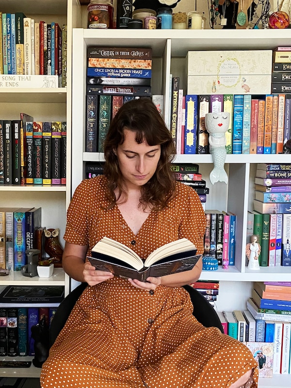 一个女人在一条长裙坐在椅子上,看书。在她身后的墙上是一个书架,装满了书。