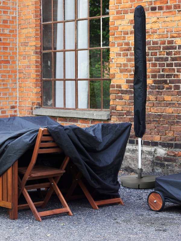 户外木桌子和椅子,存储在一个黑人旁边盖砖建筑一个窗口和收拢的阳伞。