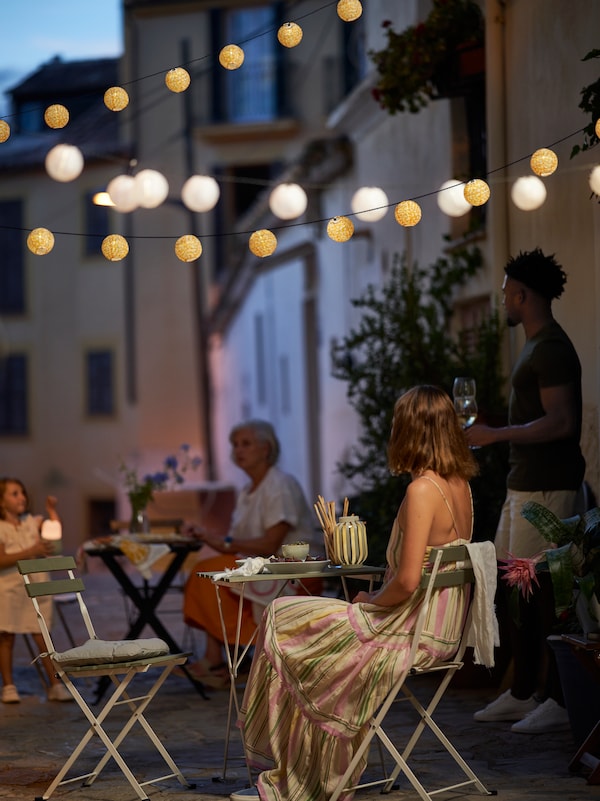 有些人在露天咖啡馆TARNO桌子和椅子在晚上与LED照明链挂上面。