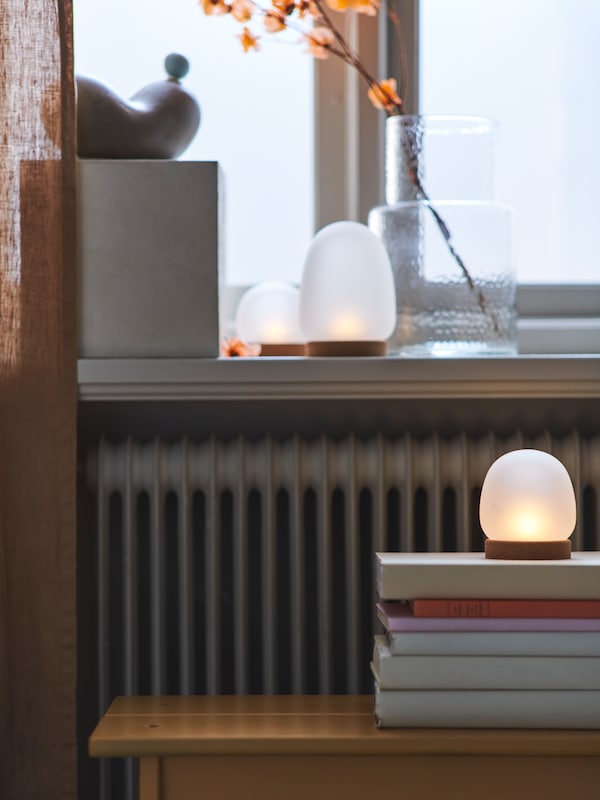 一盏灯从4件PRAKTSPIREA LED装饰照明设置站在两个相似的灯在窗台附近的一些书。
