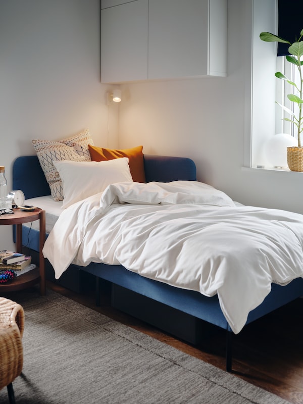 Knisa中等蓝色软垫床床头板框架角落,白色被罩和枕套和缓冲。