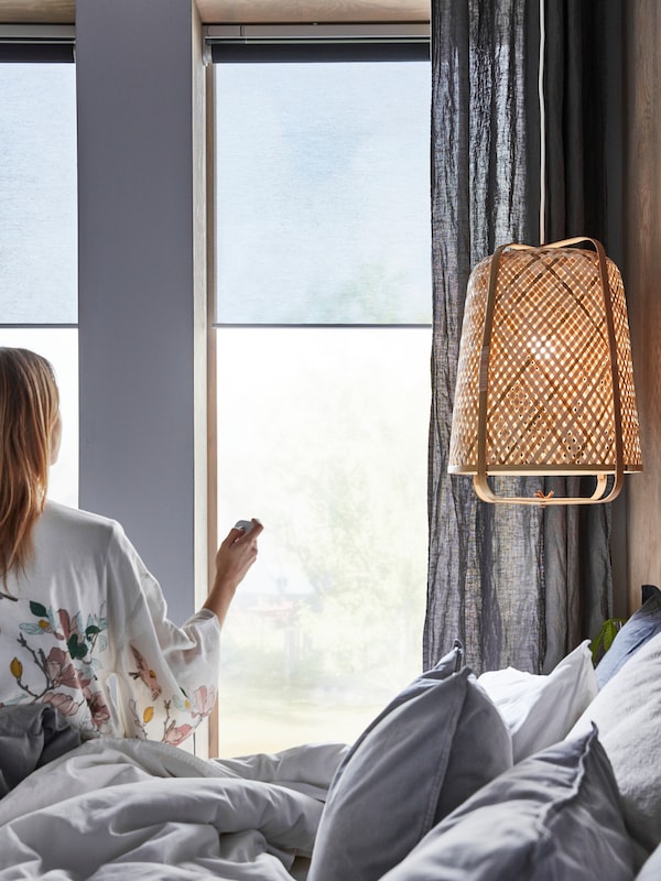 附近的一个女人,在床上KNIXHULT吊灯,使用远程控制KADRILJ卷帘挂在窗户。